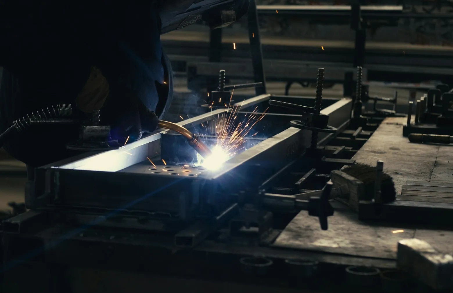 Welder joining steel on a factory workbench, sparks flying